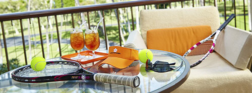 Mauna Kea tennis rackets, sunvisor, and iced tea on a glass table