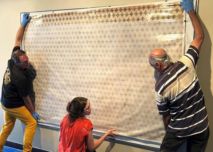 People installing a piece of artwork on a wall