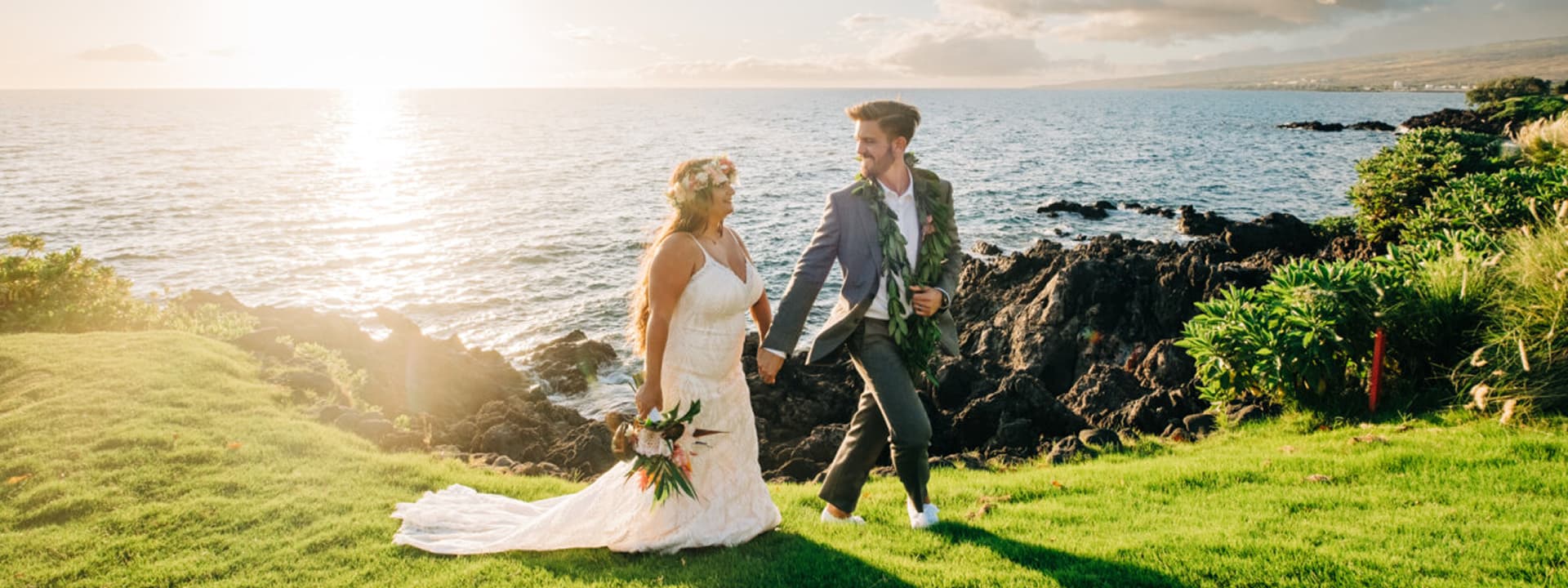 A bride and groom walk along the shore